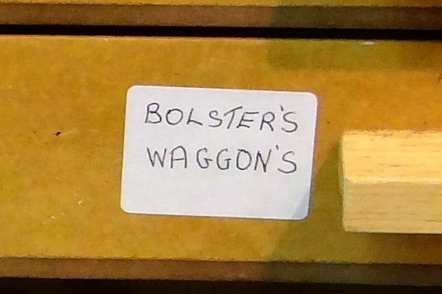 A drawer label in his hand reading “BOLSTER’S WAGGON’S”.
