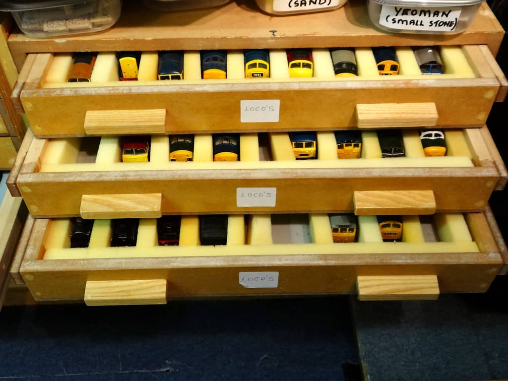 Three open drawers, each labelled LOCO’S, holding rows of model locomotives front-first in pale yellow foam, with tubs of wagon loads on the shelf above.