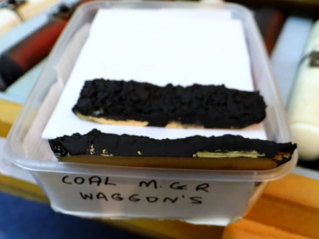 A clear tub labelled COAL M.G.R WAGGON’S with two strips of coal load on white sheets, slightly out of focus.